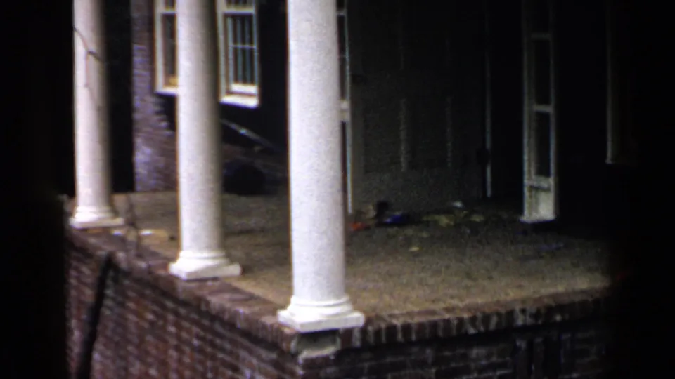 1957 Birmingham frame of the house porch corner, with white columns, brick base, a dark doorway, side windows, and low nighttime visibility.