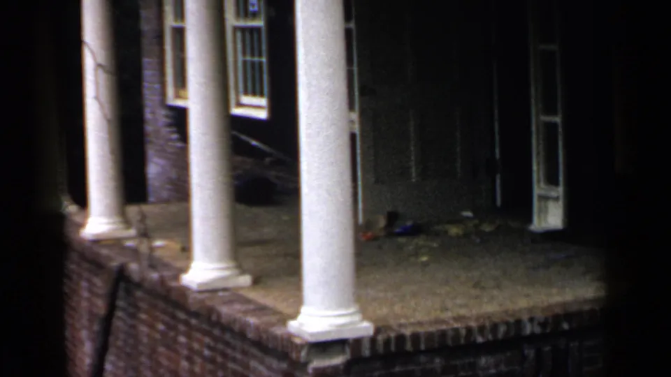 1957 Birmingham 8mm frame showing a closer nighttime view of two white porch columns, brickwork, a dark entry, and adjacent windows.
