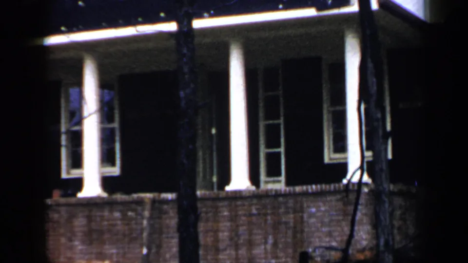 1957 Birmingham home-movie frame with the camera shifted across a brick house front at night.