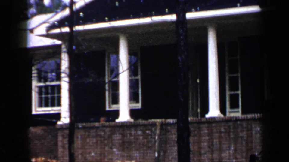Brick house exterior in Birmingham, Alabama, with porch columns and windows partially obscured by trees in 1957 footage.