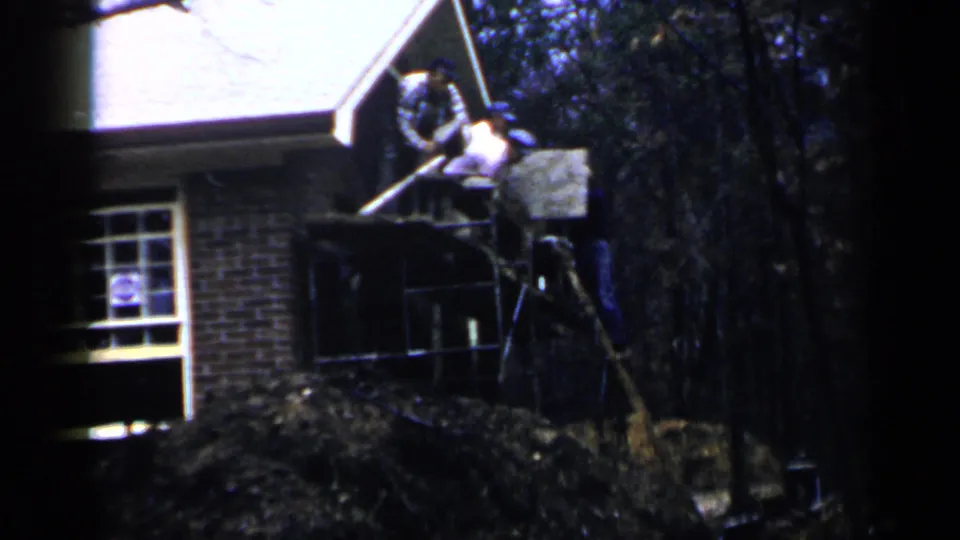 Men on ladders work near the roofline of a brick house in 1957 Birmingham home-movie footage.