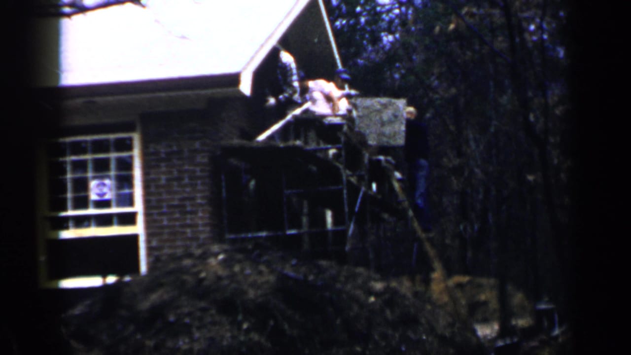 Men work on scaffolding beside a brick house under a white roof edge.