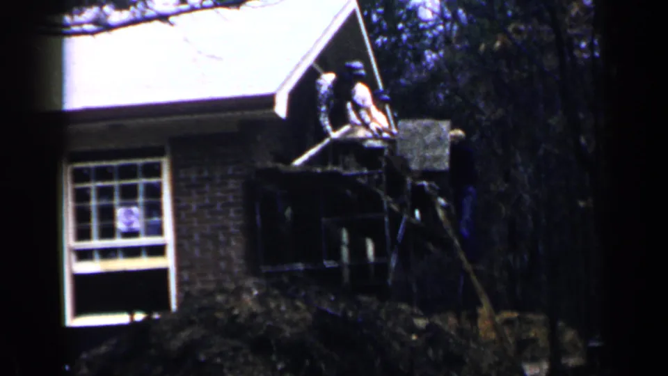 1957 Birmingham residential construction view with workers on scaffolding near the roofline of a brick house.