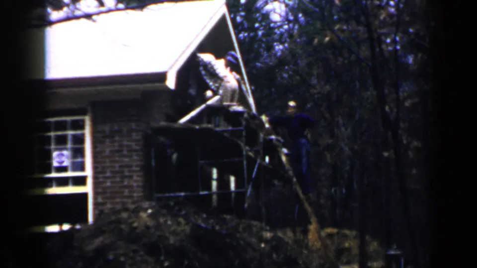 A brief 8mm frame shows men working from scaffold boards at the second story of a Birmingham brick house in 1957.