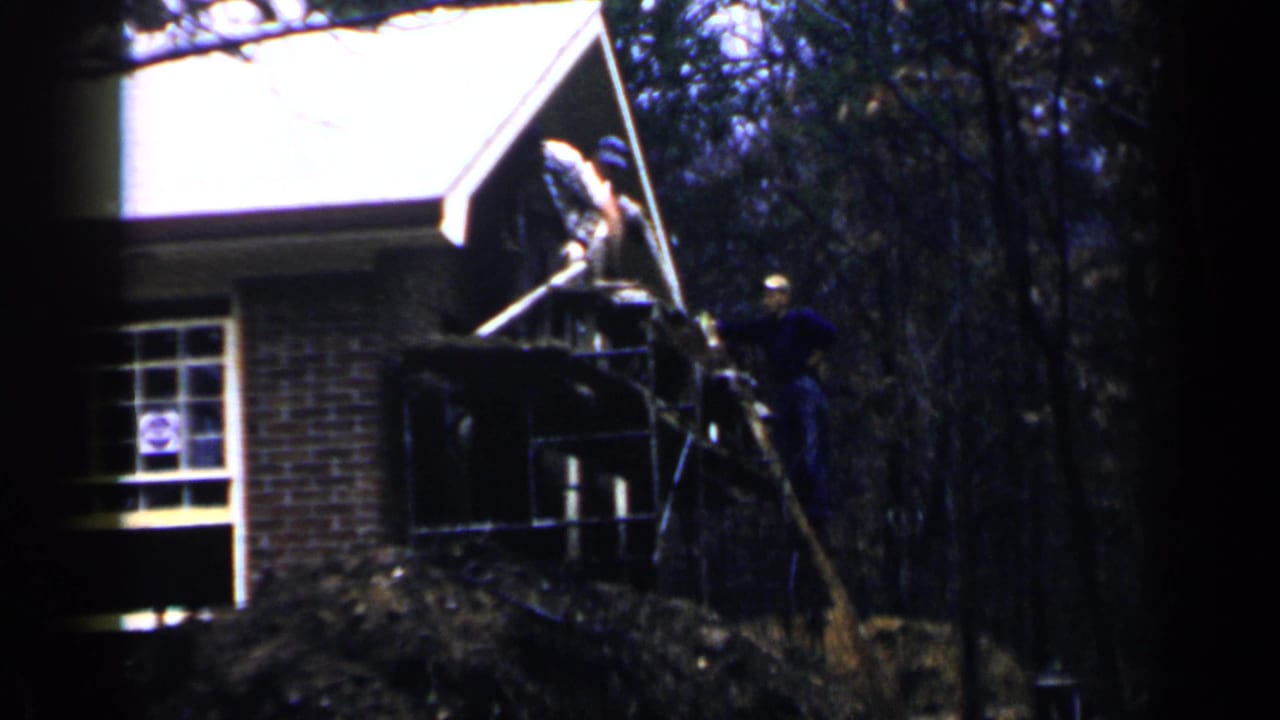 Men working on scaffolding beside a brick house porch with trees behind them.
