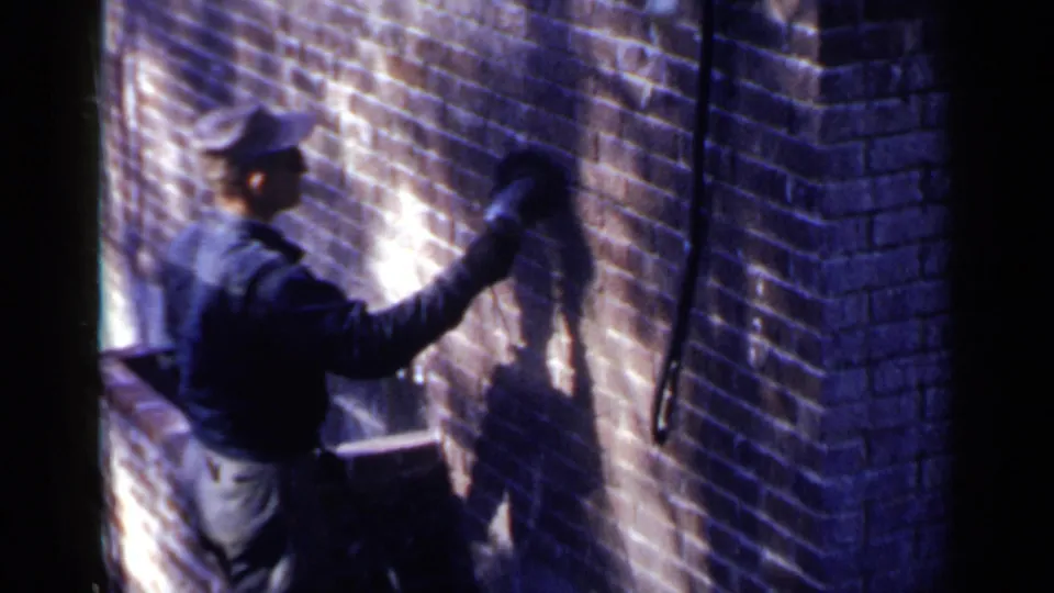 The worker holds the tool higher on the Birmingham brick wall, with his shadow sharply cast across the masonry.