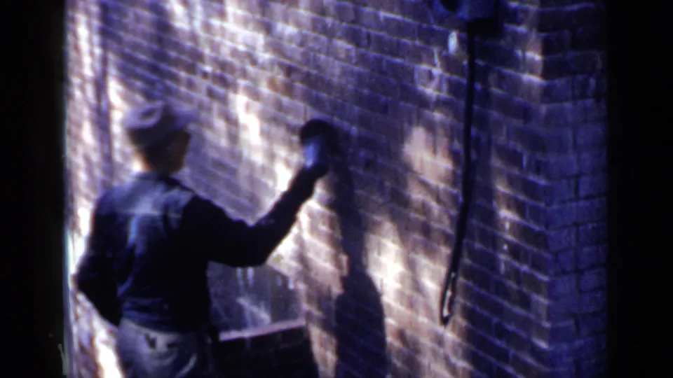 A mid-century 8mm frame shows the worker from behind as he continues cleaning or sanding the brick surface.