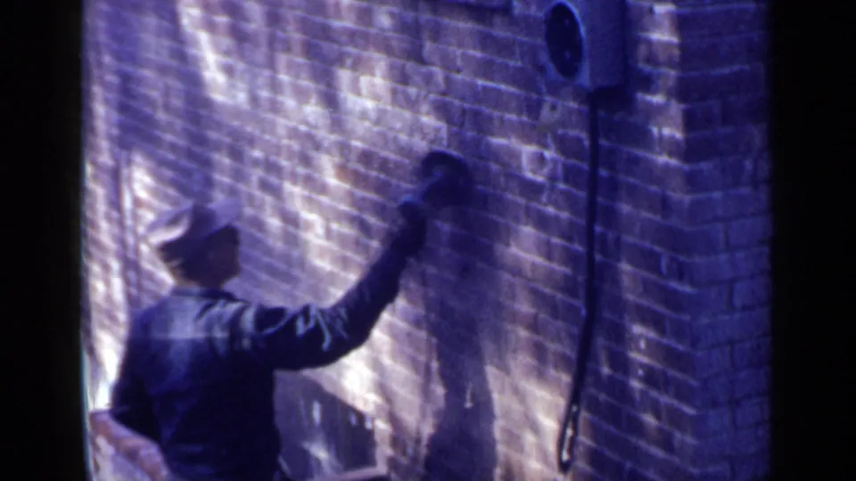 The Birmingham home-movie frame shows the worker from behind, arm raised as the tool meets the brick wall.