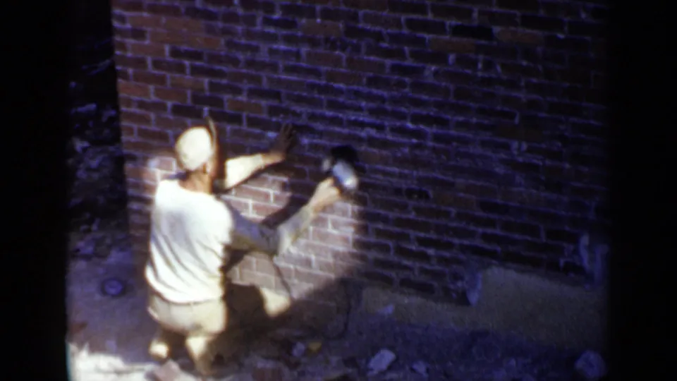 At the end of the clip, the worker continues sanding the Birmingham brick wall, seen from above with film grain and heavy contrast.
