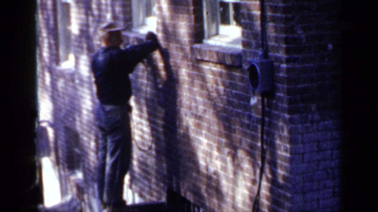 Man stands close to a brick wall, holding a tool near the surface.