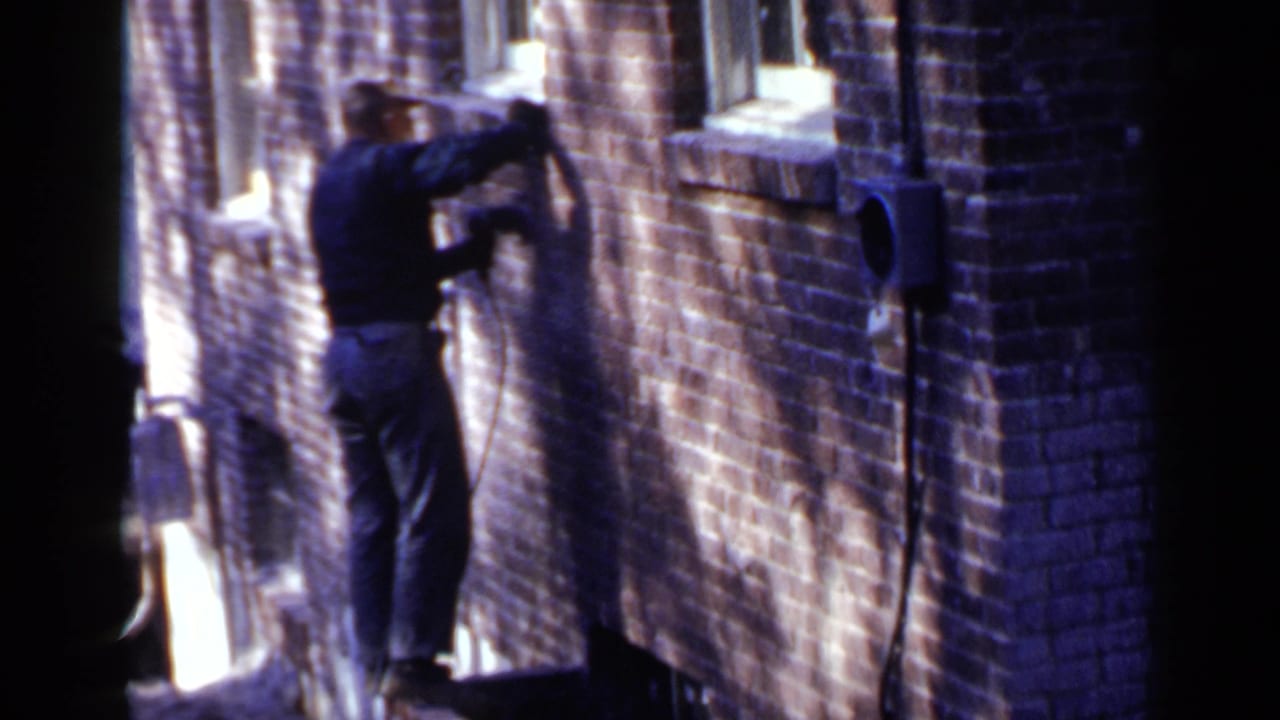 Man in dark clothing leaning toward a brick wall in a narrow alley.