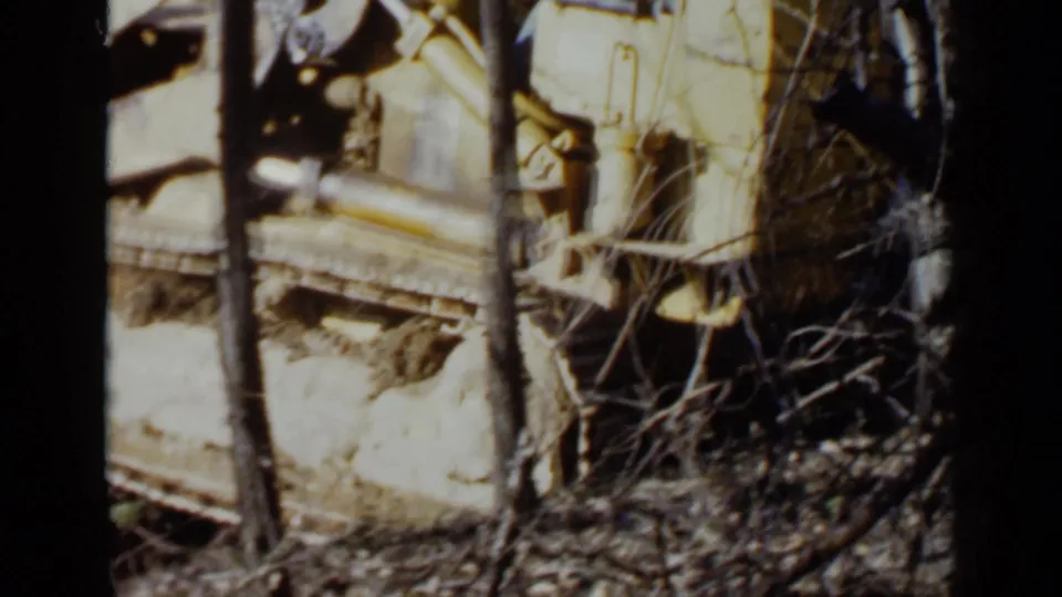 A yellow tracked bulldozer appears among bare trees and brush in the 1957 Birmingham home-movie footage.