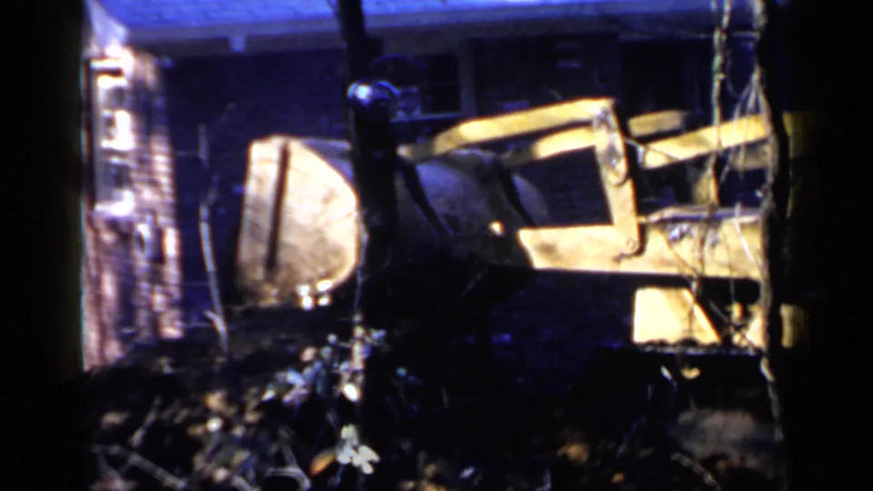 1957 Birmingham 8mm frame showing a pale weathered wooden structure amid bare branches, debris, and deep blue shadows.