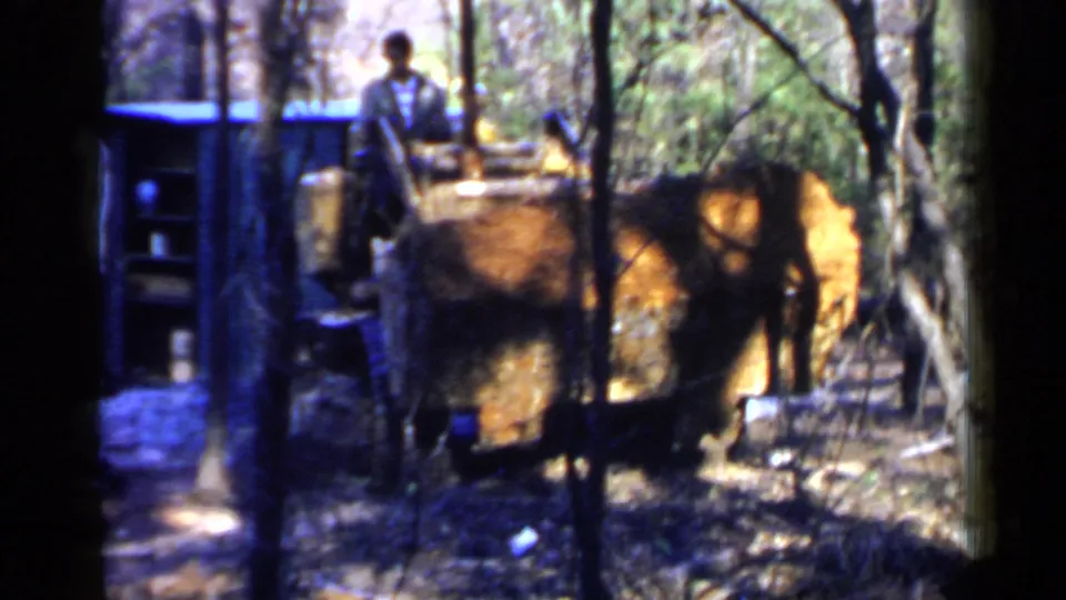 1957 Birmingham-area 8mm frame showing a man by excavation machinery among dense trees and dirt.