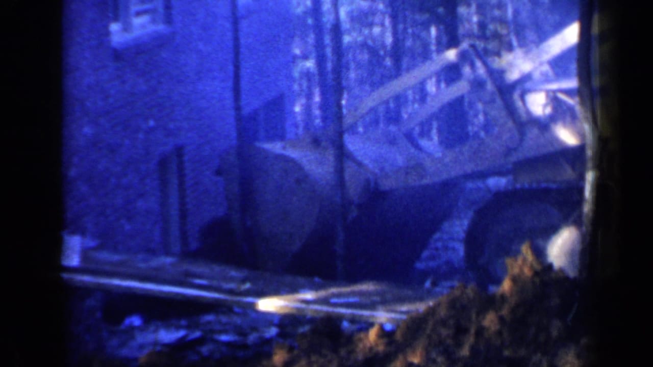 Bulldozer beside a building with its bucket near a mound of dirt.