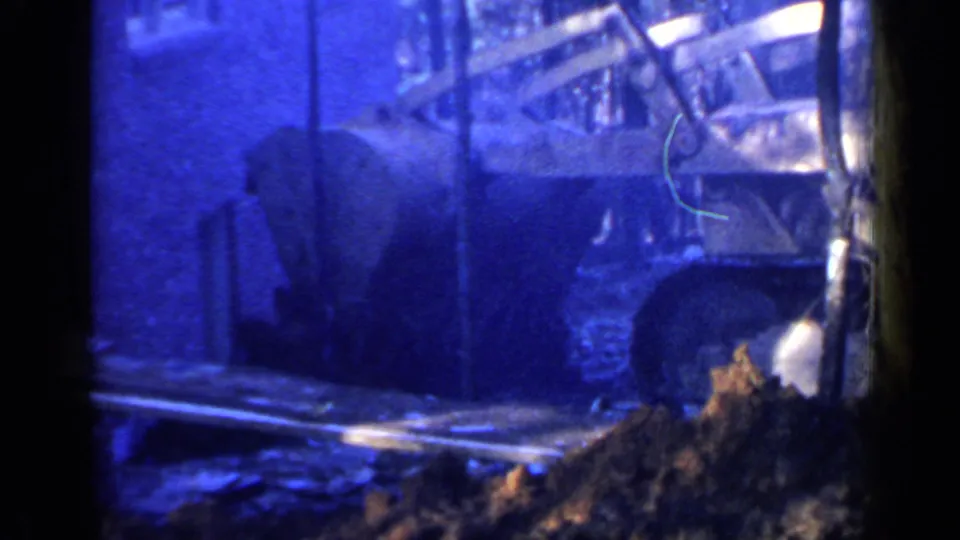 Blue-shifted 8mm view of a bulldozer near dirt and wood framing at a Birmingham construction site.