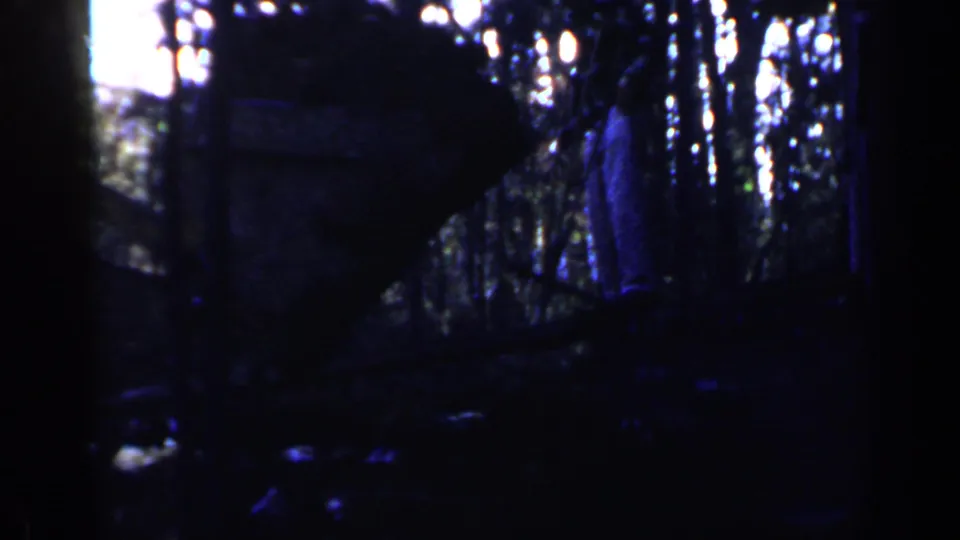 1957 Birmingham 8mm frame showing dark construction equipment in woods, with a possible distant standing figure near the right edge.