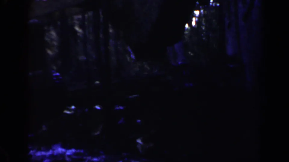 A very dark 8mm frame from the Birmingham clip shows faint machinery or site structures with blue highlights and heavy grain.