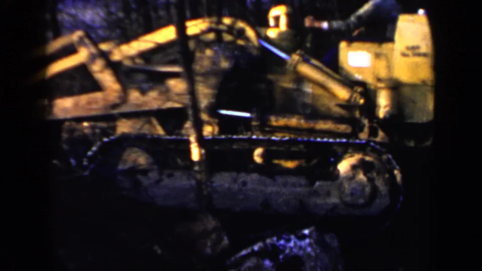 Birmingham, Alabama 1957 frame showing yellow tracked heavy equipment clearing a wooded site, with crawler tracks, blade arm, brush, and a possible operator.