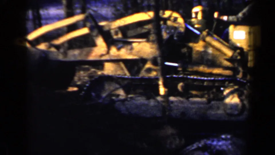 1957 Birmingham-area home-movie frame showing a yellow tracked tractor moving through a wooded area on red earth.