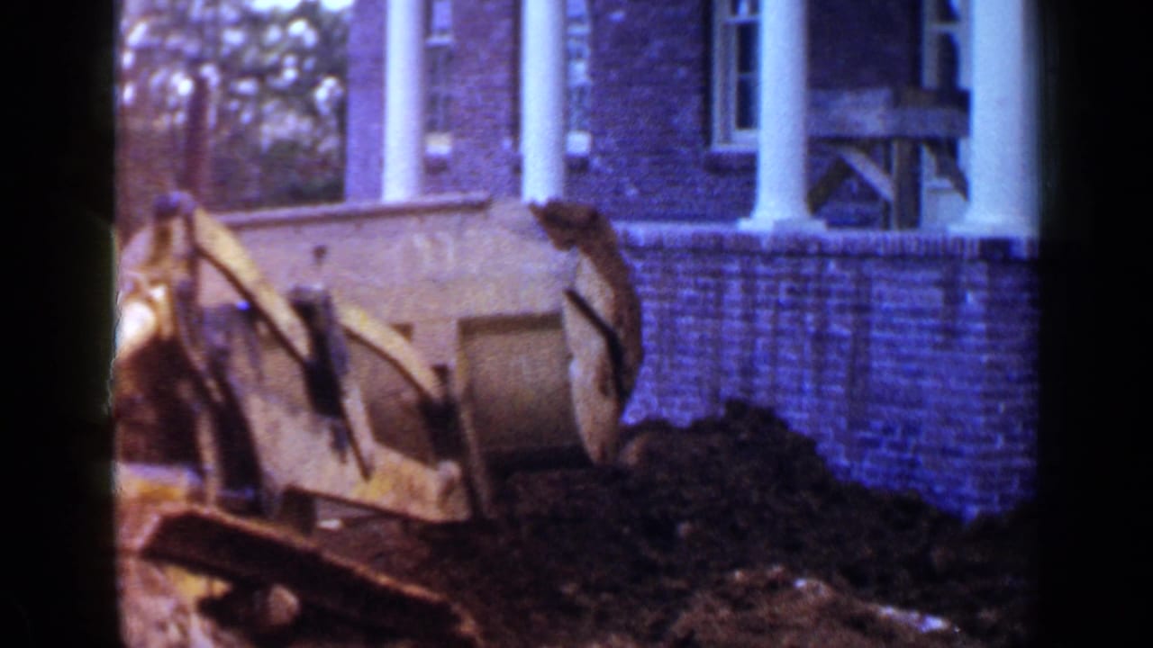Yellow bulldozer beside a dirt pile in front of a brick house with white columns.
