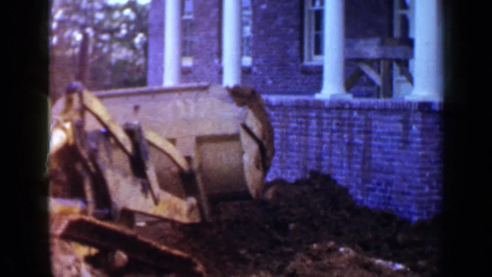 1957 Birmingham home-movie frame showing a yellow bulldozer working near a brick house and dirt pile.