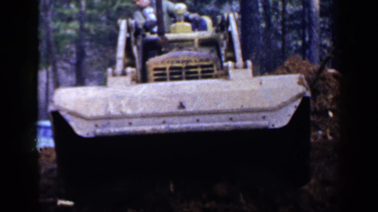 Yellow bulldozer facing the camera in a wooded construction area.