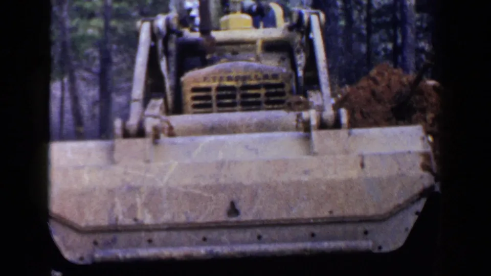 Yellow crawler bulldozer in a wooded Birmingham-area construction scene, with the operator faintly visible above the blade.
