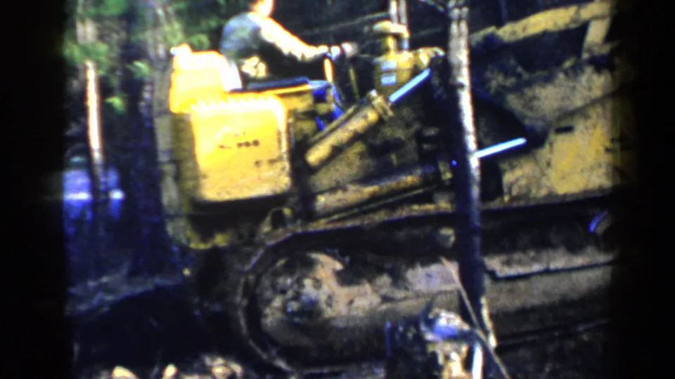 Close home-movie view of the yellow bulldozer body, muddy tread, and nearby trees during the 1957 Birmingham scene.