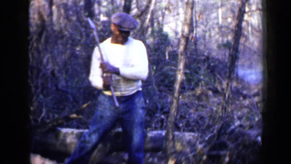 The man stands in a wooded Birmingham setting, holding a long-handled tool as the 8mm frame catches soft focus and color shift.
