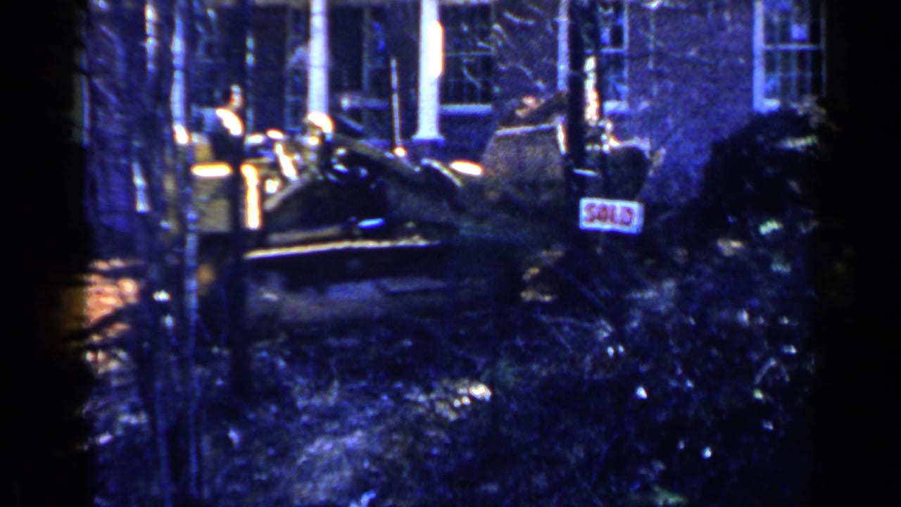 Bulldozer partly obscured by trees beside a house with a SOLD sign nearby.