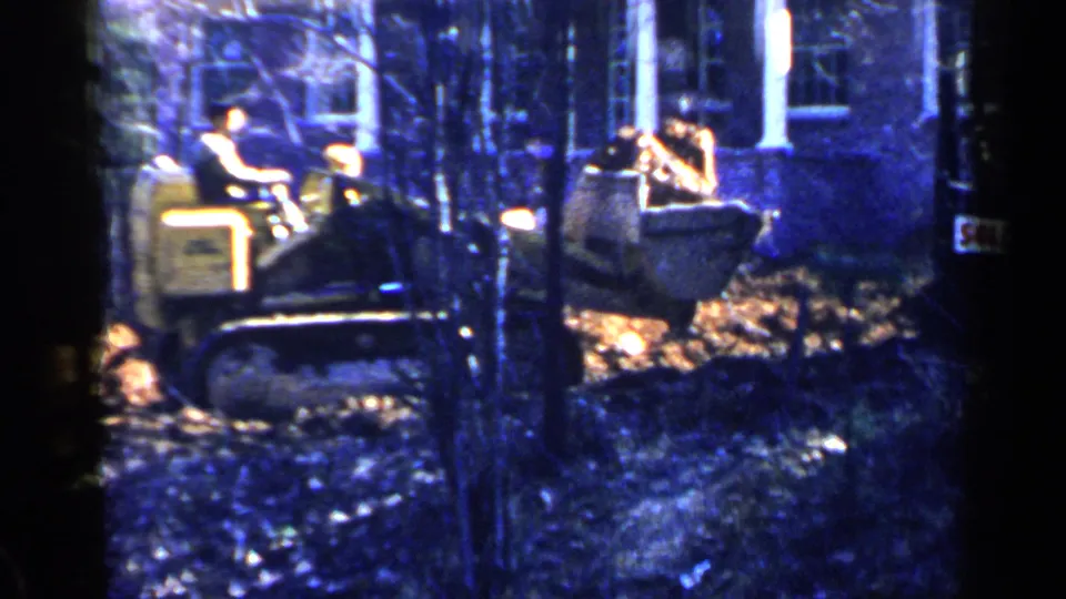 1957 Birmingham footage frame with a man seated on a vintage crawler bulldozer clearing ground near a residential house.