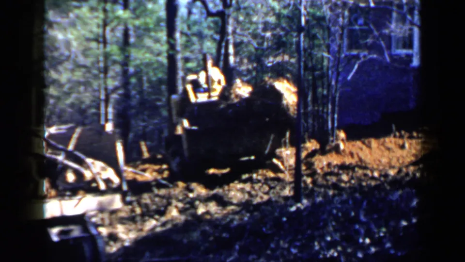 1957 Birmingham-area home-movie frame of a bulldozer pushing material near trees, with part of a structure visible in the background.
