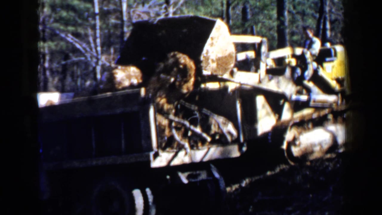 Earthmoving machine and dump truck remain side by side as rocks sit in the truck bed.