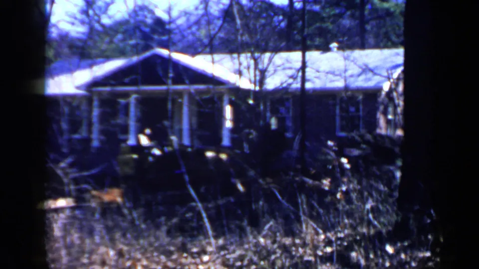 Wooded 1957 Birmingham-area frame with a modest cabin-like structure partly obscured by trees and dark foreground equipment.