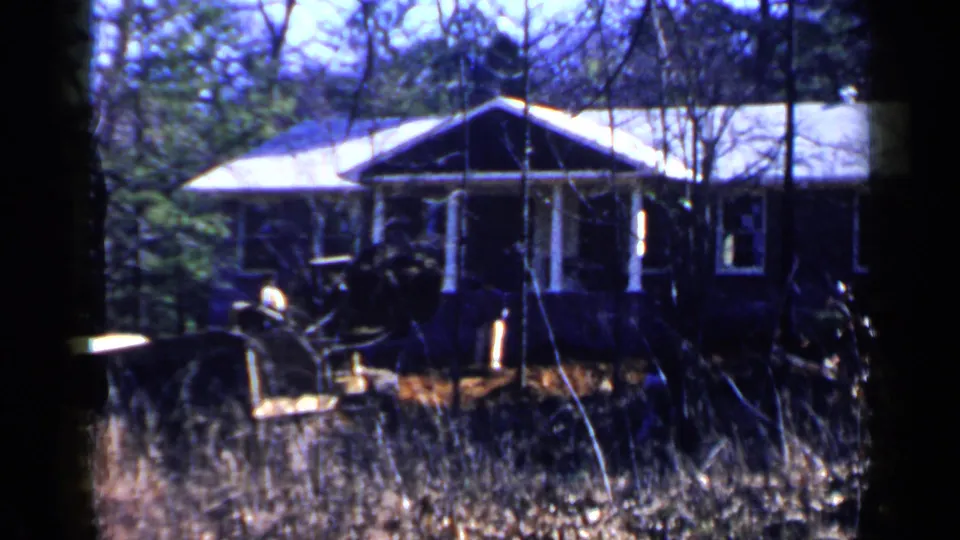 1957 Birmingham 8mm view of a brown house with porch columns as a yellow bulldozer sits or moves in the overgrown yard.