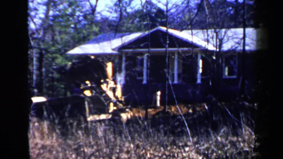1957 Birmingham frame with a yellow brush-clearing vehicle positioned beside a small porch-front house.