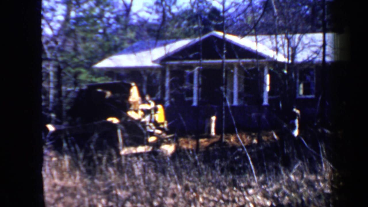 Yellow construction vehicle in front of a small house among trees.