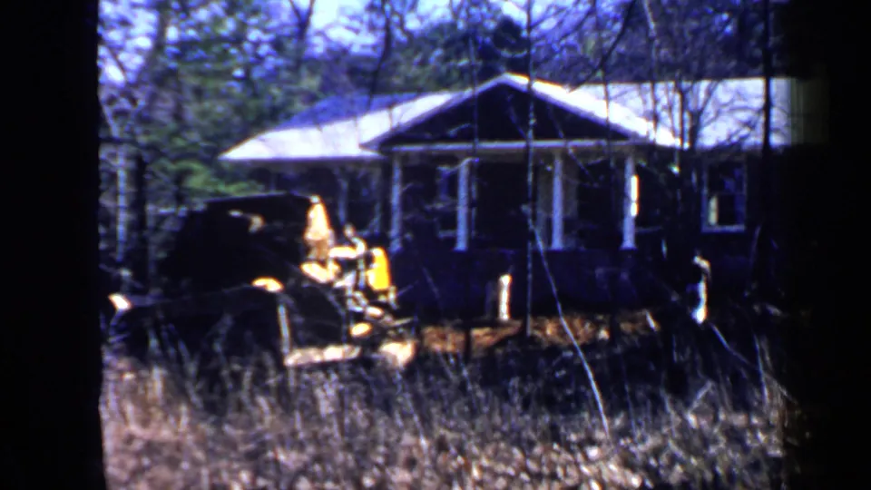 1957 Birmingham home-movie frame showing a yellow construction vehicle near a single-story house in a wooded yard.