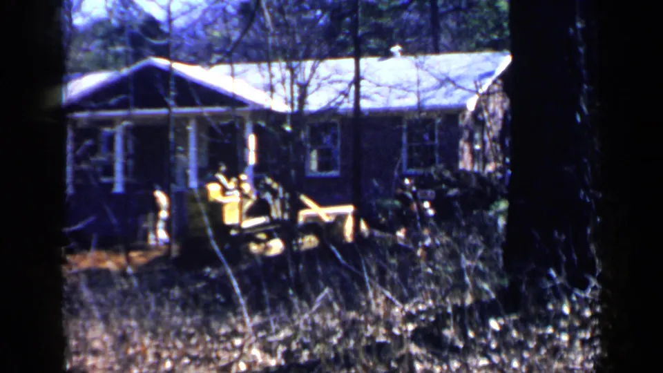 Yellow high-lift loader appears beside a wooded residential exterior in 1957 Birmingham, Alabama footage.