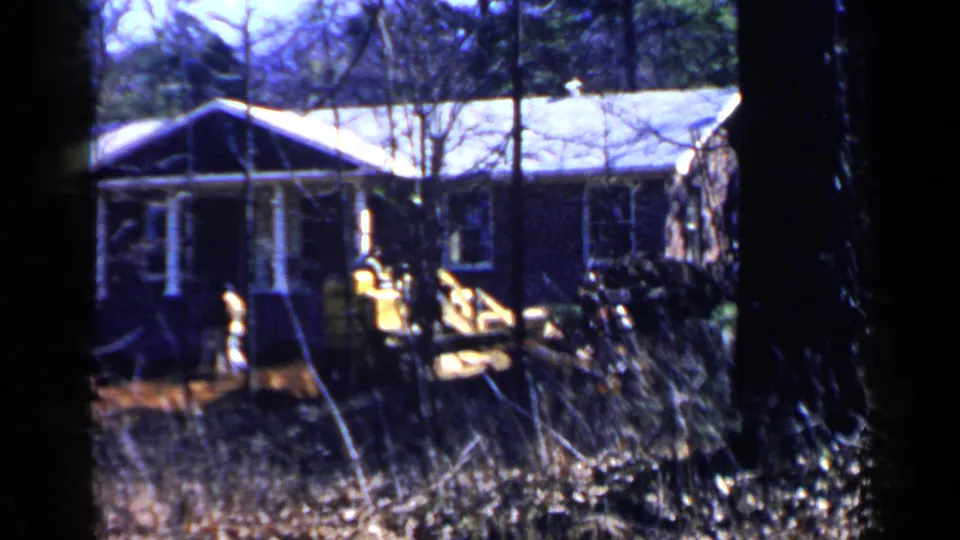 1957 Birmingham home-movie frame with a yellow loader and operator near a residential house exterior.