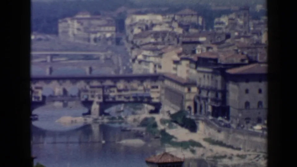 Soft 8mm frame of Florence's Ponte Vecchio and the Arno River, with stone embankments and clustered buildings in view.