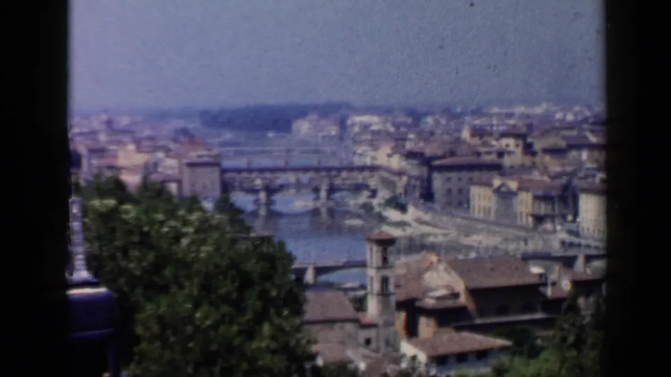 Wide visitor-shot view of Florence with the Arno River, Ponte Vecchio area, rooftops, trees, and distant city skyline.