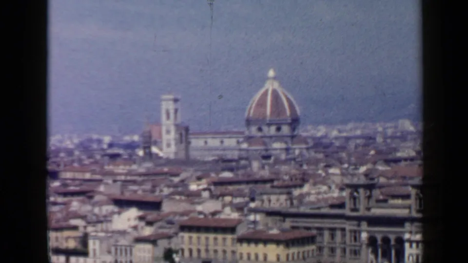Wide 1960s 8mm cityscape of Florence with the cathedral dome, bell tower, roofscape, and hazy hills beyond.
