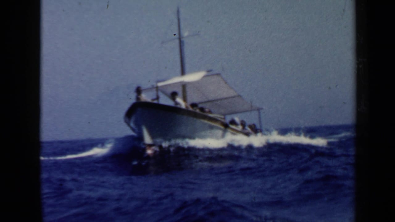 Small motorboat with passengers and a white canopy moving through blue waves.