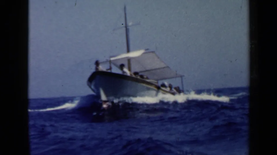 A small motorboat carrying visible passengers cuts across choppy blue water under a simple white canopy.