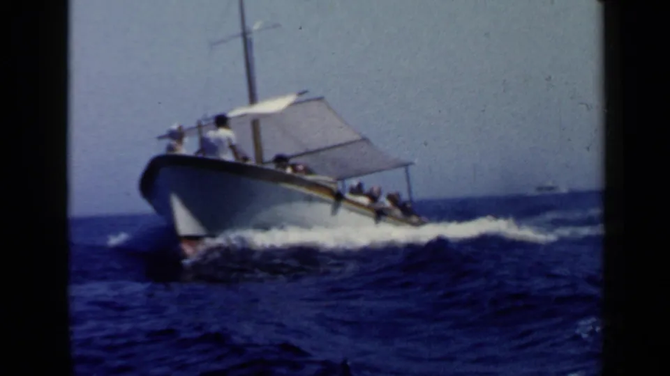 Close 1960s 8mm view of a small passenger motorboat pushing through waves, with its canopy and dark hull visible.