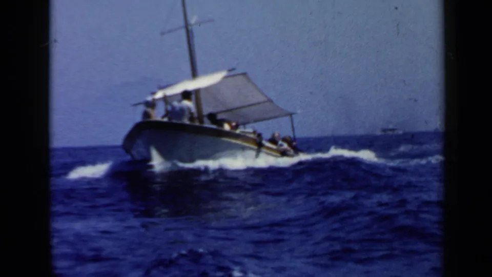1960 Rome-area 8mm frame of a small canopy tour boat moving across rough blue water with passengers aboard.