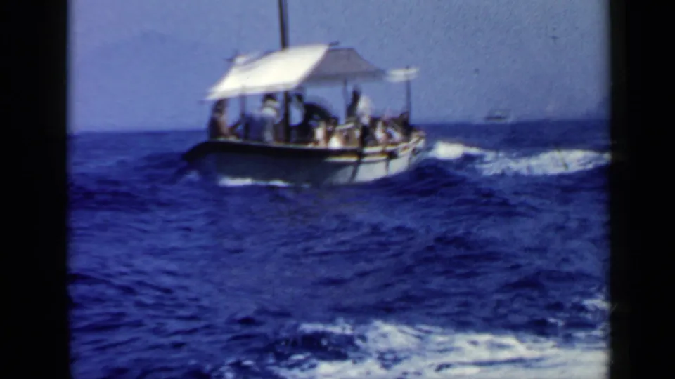 A canopy-covered passenger boat moves over choppy water in 1960 Rome-area travel footage.