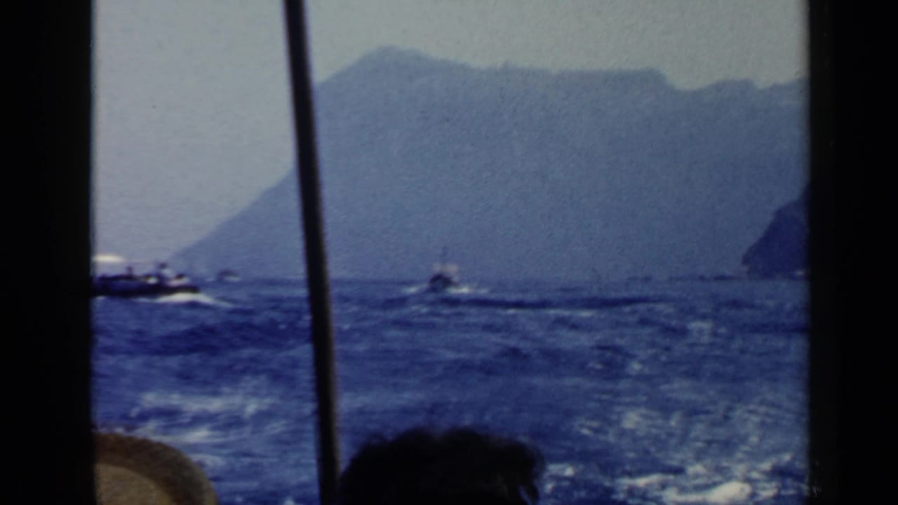 Boat wake on blue water with mountains and shoreline in the distance.